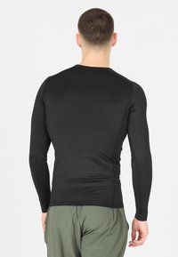 Zwarte langemouwen shirt van rekbare stof, met een ronde halslijn en een aansluitend ontwerp. Gecombineerd met lichtgroene sportbroeken.