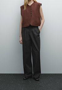 Brun nubuck, ärmlös topp med rundad halsringning och knapplist, kombinerad med högmidjade, mörkgrå vida byxor.