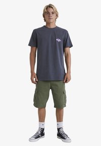 Dark gray cotton t-shirt with pink graphic, paired with olive green cargo shorts, white socks, and black high-top sneakers.