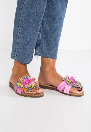 Pieds portant un jean bleu court et des sandales à glissière roses avec de grandes décorations florales en tissu multicolore sur le dessus.