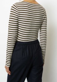 Randig långärmad topp i olivgrön och krämfärgad, med en bred halsringning, tillsammans med mörka byxor med elastisk midja och sidoficka.