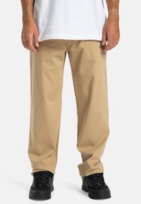 Beige rechte broek gemaakt van katoen, met een eenvoudig ontwerp en een gladde textuur. Gemaakt om te dragen met zwarte sneakers met textuur.