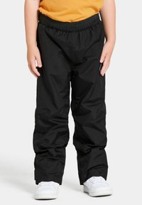 Mustat vedenpitävät housut, joissa on elastinen vyötärö, rento malli ja sivutaskut, yhdistettynä valkoisiin tennareihin ja keltaiseen paitaan.