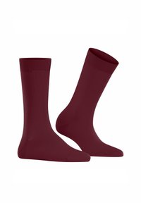 Deux chaussettes bordeaux présentées à la verticale, mettant en avant leur texture lisse et leur couleur unie, avec un haut côtelé et un design sans couture.