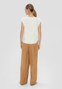 Blouse blanche ample à manches courtes, associée à un pantalon large beige. Texture de tissu douce, coupe droite et ajustement décontracté.