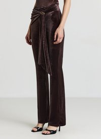 Pantaloni di velluto marrone scuro con davanti drappeggiato e dettaglio dorato. Design aderente, svasati nella parte inferiore, abbinati a sandali neri open-toe.