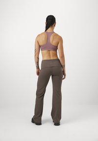 Sportowy stanik w stonowanym różowym kolorze, z tyłem typu racerback. Dopasowane brązowe spodnie z szerokim paskiem. Oba wykonane z elastycznego materiału.