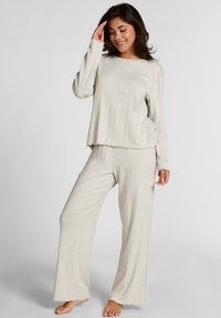 Lichtbeige langemouwen top met ribbeltextuur en golvende zoom, gecombineerd met een wijde broek in vergelijkbaar materiaal en kleur.