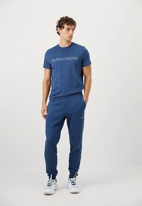 Plava pamučna majica s natpisom "BJÖRN BORG" sprijeda, u kombinaciji s pripadajućim plavim trenirkama. Oba komada imaju glatku teksturu i ležeran kroj.