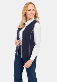 Marineblauer Weste mit grauen Nähten, ausgestattet mit einer geknöpften Vorderseite und einem lässigen Schnitt. Getragen über einem weißen Hemd mit blauen Jeans. Glatte Textur.