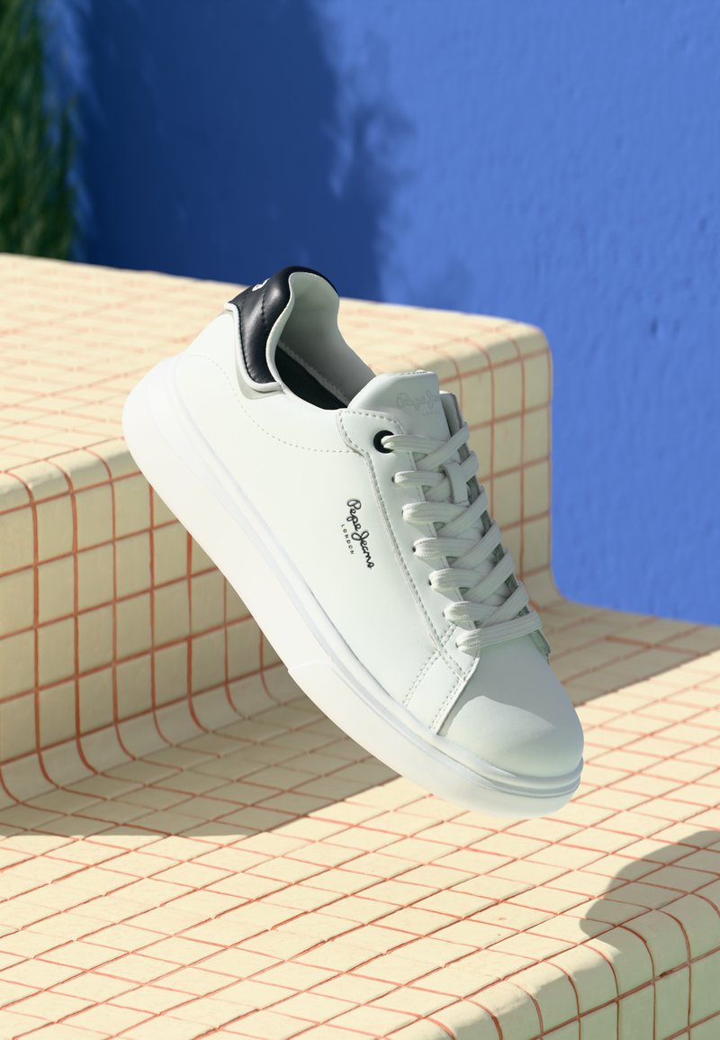 Adidași albi cu talpă joasă, cu toc negru, șireturi și logo-ul "Pepe Jeans London", expuși pe o suprafață de gresie bej, cu un fundal albastru.