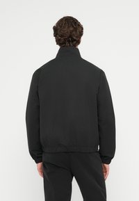 Sort, letvægtsjakke med høj krave, elastiske manchetter og kant. Glat tekstur, enkelt design og ingen synlige mønstre eller hardware.