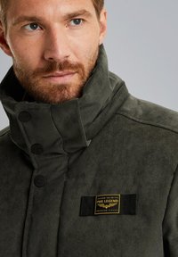 Donkergroene corduroy jas met een hoge kraag, voorzien van zwarte knopen en een verweerd label met de tekst "PME Legend American Classic."