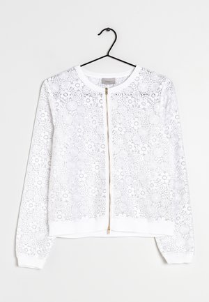 Sweat à zip blanc avec empilage de dentelle florale, manches longues, poignets et ourlet côtelés, et une fermeture éclair dorée. Conçu avec des accents minimalistes.