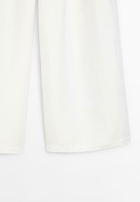 Culottes en lin blanc avec une coupe ample, des jambes larges et des détails de couture à l'ourlet. Texture douce et matériau respirant, idéal pour les temps chauds.