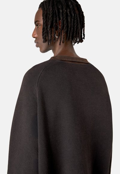 Dunkelbrauner Pullover mit lockerer Passform, rundem Ausschnitt und geripptem Kragen. Das Material scheint weich und strukturiert mit sichtbaren Nähten zu sein.