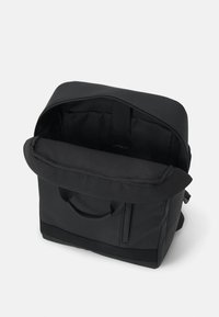 Svart tygväska med dragkedja på toppen, handtag och en innerficka. Slät textur med en strukturerad form. Minimalistisk design, ingen synlig branding.