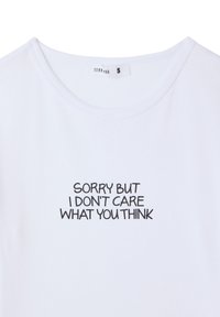 T-shirt bianca in cotone con scollatura tonda, decorata con testo nero: "MI DISPIACE MA NON MI IMPORTA DEL TUO PENSIERO." L'etichetta della taglia indica 'S.'