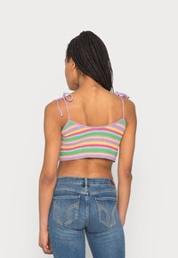 Top de malha cropped em riscas verde pastel, rosa e lavanda, com alças de ombro com laço e um acabamento texturizado. Usado com jeans azuis.