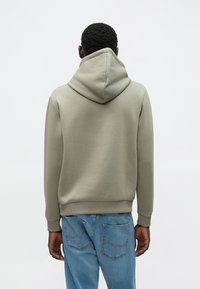 Lys grønn hettegenser med avslappet passform, ribbestrikkede mansjetter og kant. Brukt sammen med blå jeans med detaljering på baklommene.