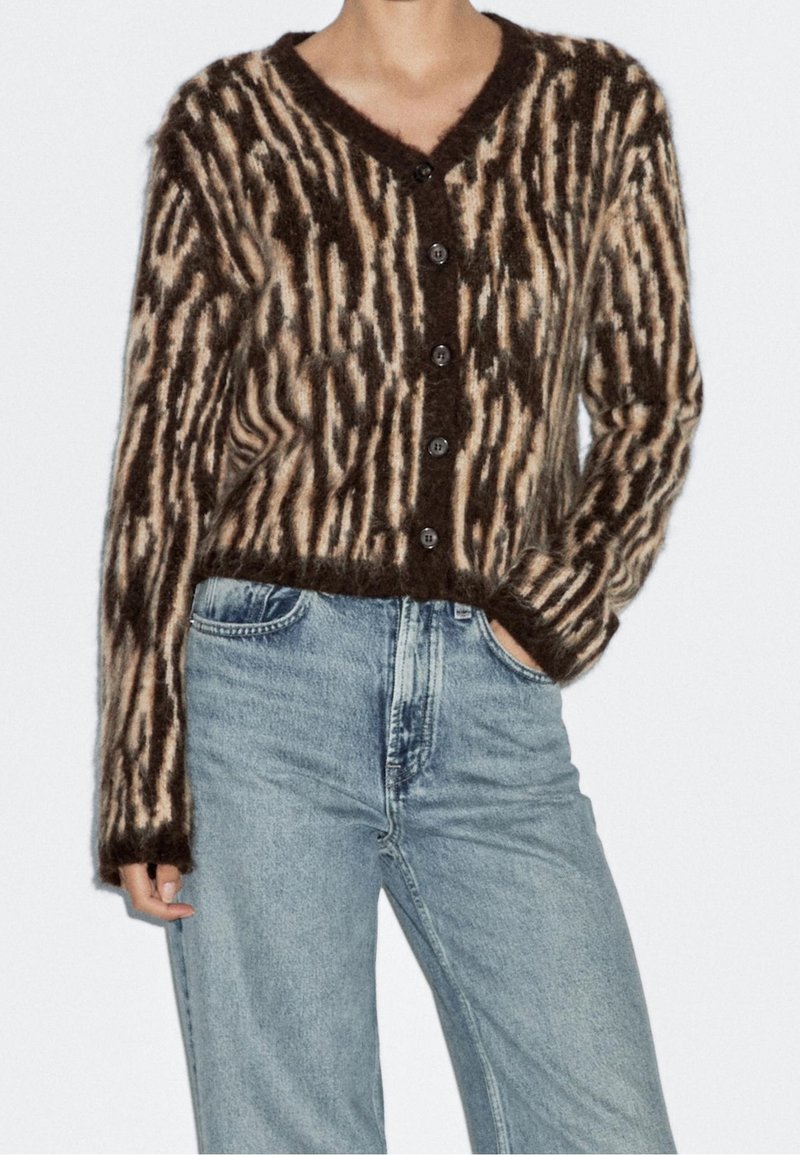 Personne portant un cardigan boutonné et duveteux avec un imprimé animal marron et beige associé à un jean taille haute bleu clair.
