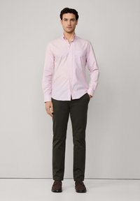Camisa de cuadros rosa, de botones, de manga larga, combinada con pantalones oscuros verdes. Corte slim, con cuello y detalle de bolsillo en el pecho. Calzado marrón.