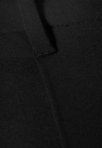 Black stretchy fabric featuring a textured surface and a neat seam. Contains a small, looped tag for potential hanging or adjustment.
