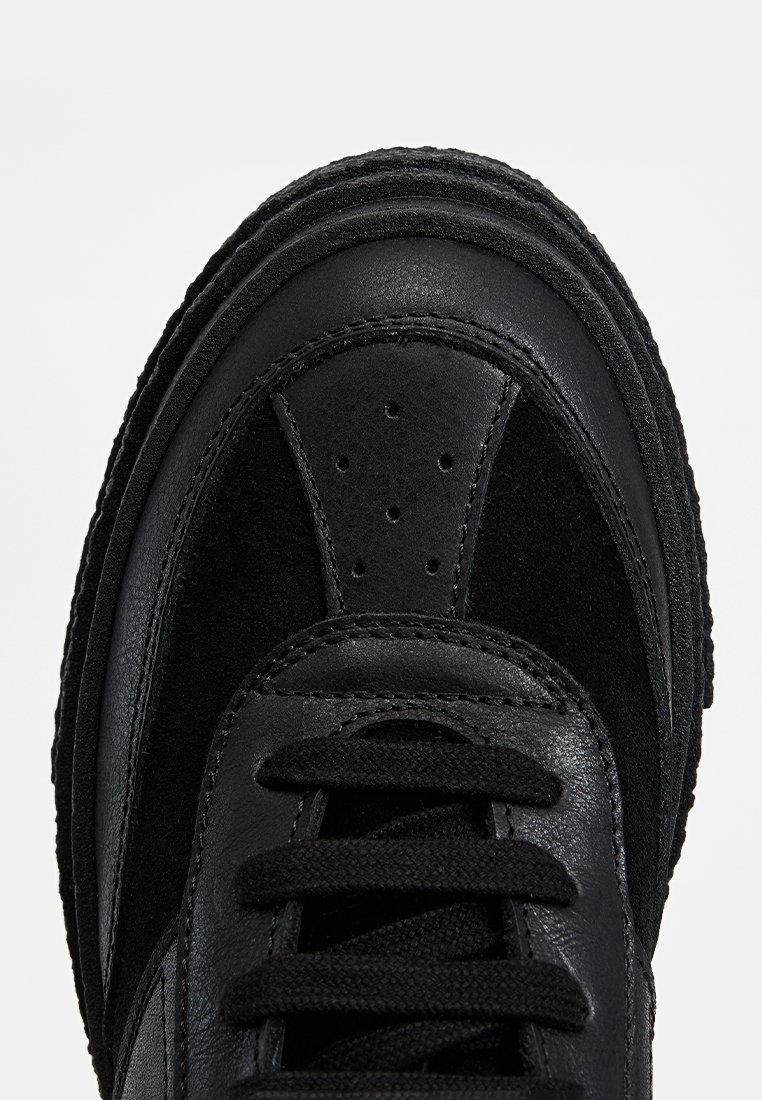 Sneaker nero con tomaia in suede testurizzato e pelle liscia, punta arrotondata, sei occhielli con lacci e dettagli di cuciture evidenti.