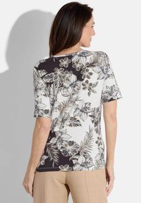 Blumige Bluse mit kurzen Ärmeln; verfügt über ein schwarz-weißes Blumenmuster mit beige Akzenten. Weicher Stoff; lockere Passform; runder Halsausschnitt.