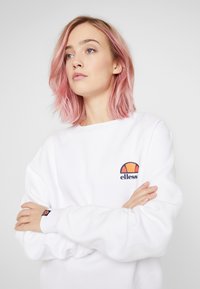 Sudadera blanca con un logo en naranja y marino, cuello redondo y mangas con puños, fabricada con un tejido suave y de corte holgado.