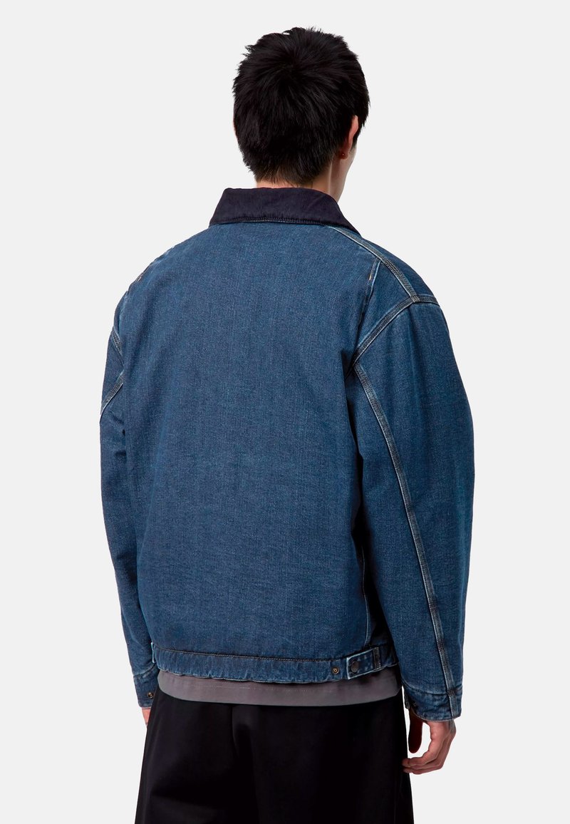 Giubbotto in denim dal design classico, con colletto scuro, ampia spalla posteriore e cuciture visibili, presentato in un blu medio.