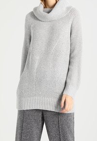 Grå stickad tröja med en cowl-halsringning, ribbad textur och en avslappnad passform. Något längre bak för extra komfort. Matchas med grå byxor.