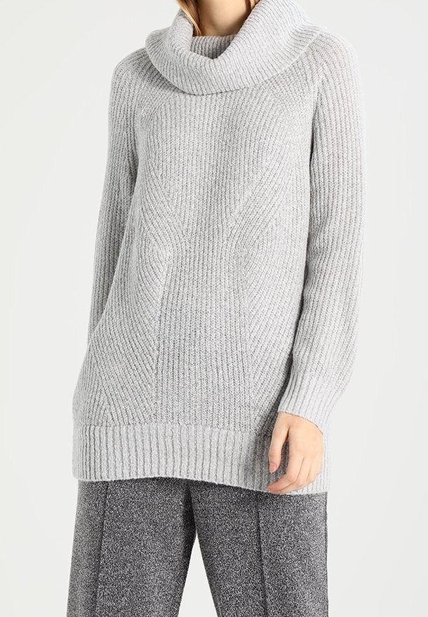 Grå stickad tröja med en cowl-halsringning, ribbad textur och en avslappnad passform. Något längre bak för extra komfort. Matchas med grå byxor.