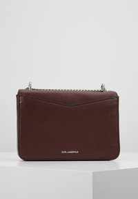 Bordeaux læder håndtaske med strukturfinish, sølvfarvet kæde-rem og geometrisk flap design. Har "KARL LAGERFELD" branding nederst.
