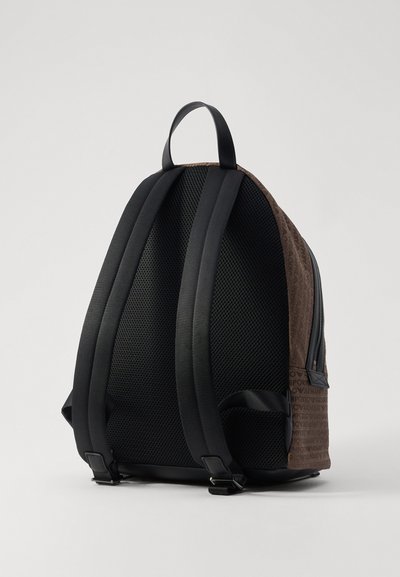 Zaino con un esterno testurizzato marrone, spallacci in tessuto a rete nera e un accento liscio. Presenta un sistema di cinturini regolabili e un scomparto con cerniera.