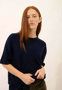 Granatowy, oversize'owy sweter z krótkimi rękawami i okrągłym dekoltem, w połączeniu z oliwkowymi spodniami z korduroyu. Widoczna miękka tekstura.