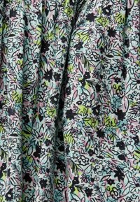 Tissu doux avec un motif floral dense en rose pastel, bleu, vert et noir sur un fond clair, présenté avec des plis.