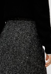 Pull noir en maille associé à une jupe en tweed noir et blanc texturé. Le tissu présente un motif moucheté et une taille.