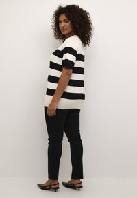 Svart och vitrandig stickad topp med korta ärmar, parat med svarta slim-fit jeans och svarta klackskor. Texturerat tyg, avslappnad design.