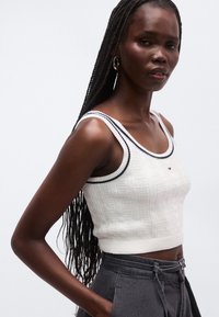 Bílý pletený crop top s texturovaným vzorem, kontrastním námořnicky modrým lemem a logem Tommy Hilfiger na přední straně.