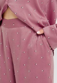 Ensemble de loungewear en satin lavande, présentant un motif de petits cœurs en blanc et noir, avec une coupe décontractée et une poche latérale visible.