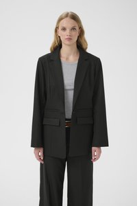 Fekete szabott blézer, hullámos gall�érral, két első zsebbel és egysoros gombolással. Szürke felső fölött viselve, az anyag simának tűnik.