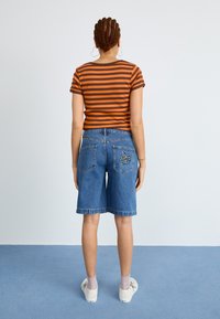 Stribet oransje og brunt kortermet topp kombinert med blå denimshorts med design på baklommene. Hvite sneakers med grå sokker.