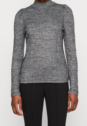 Woman wearing a fitted grey ribbed long-sleeve sweater with slight shoulder gathers and black pants, standing against a plain background.