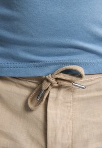 Lichtblauwe katoenen shirt met een soepele textuur, gecombineerd met beige linnen broek met een geknoopt taupekleurig trekkoord en zilveren aglet.
