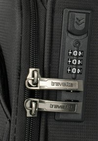 Black luggage zipper with two silver "travellite" pull tabs, featuring a combination lock with three number dials. Textured fabric visible.