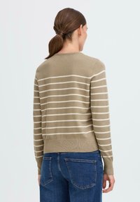 Beige genser med kremfargede striper, rund hals, ribbestrikkede mansjetter og kant. Brukt med blå denimjeans. Glatt tekstur, lett materiale.