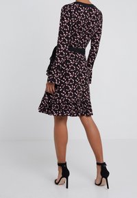 Musta mekko, jossa on vaaleanpunaisia ja valkoisia kukkia, pitkähihaiset, röyhelöalareuna ja musta vyö. Yhdistetty mustien korkokenkien kanssa.