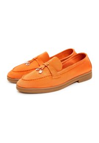 Mocassins en daim orange avec un bout arrondi, une semelle plate en caoutchouc marron et un détail décoratif en forme de nœud sur le cou-de-pied. Texture lisse sur toute la surface.