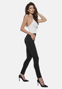 Czarne legginsy o slim fit, wysoki stan i kieszeni po boku. Połączone z białym, dopasowanym, bezrękawnikowym topem i czarnymi szpilkami.